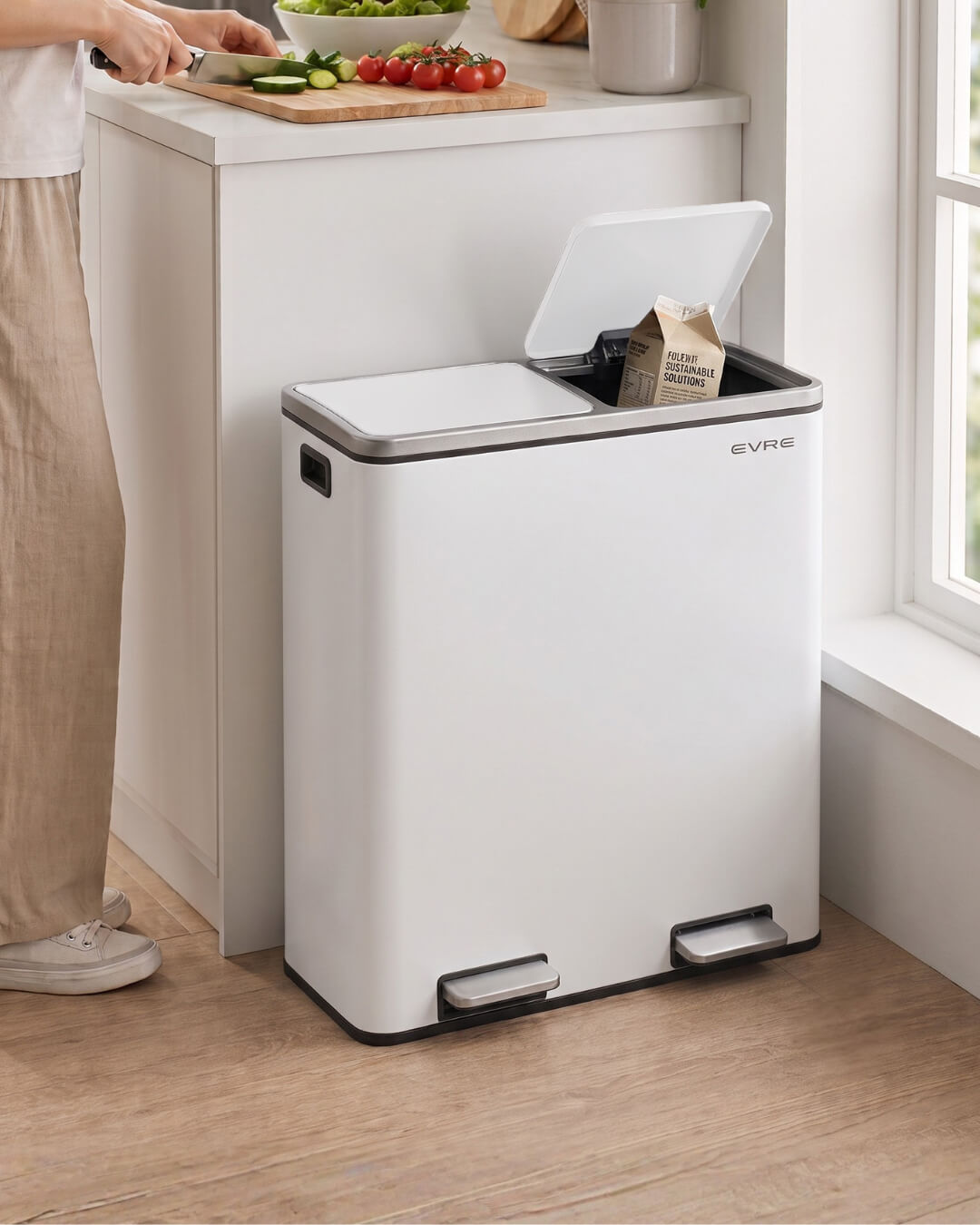 A large white dual kitchen bin with an open lid, placed on a wooden floor next to a kitchen counter