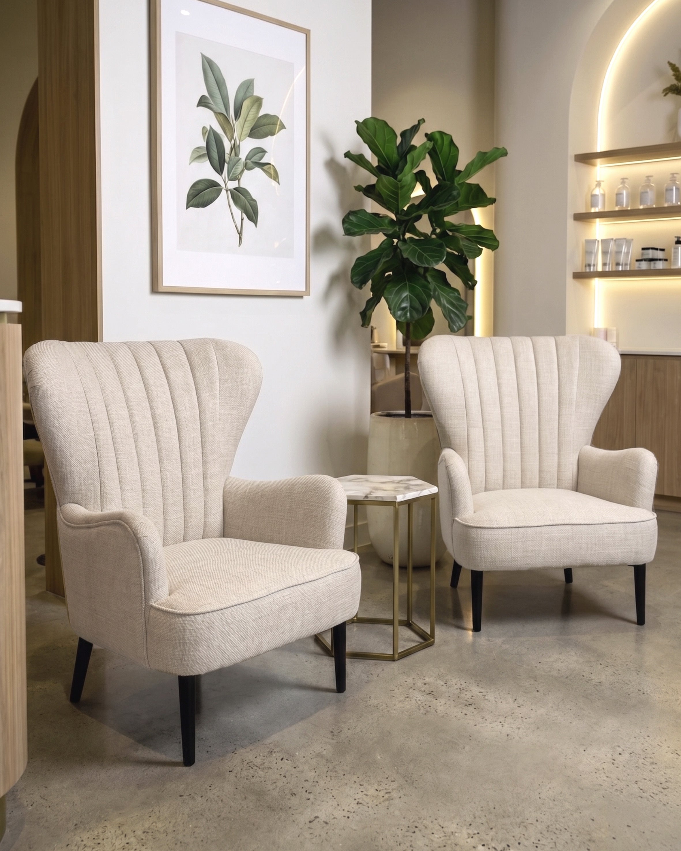 Two cream wingback armchairs in a room with a plant and framed artwork on the wall