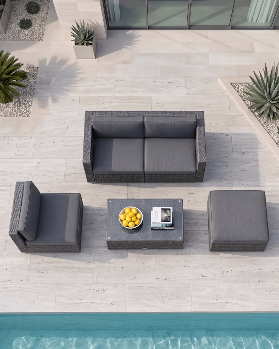 A top-down view of a 5-piece outdoor patio conversation set in dark grey wicker, including a rectangular coffee table, arranged on a light stone patio next to a swimming pool