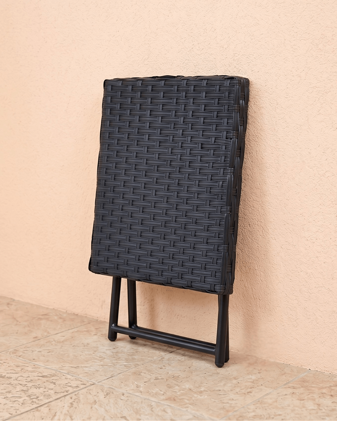 A black rattan folding garden bistro table leaning against the wall