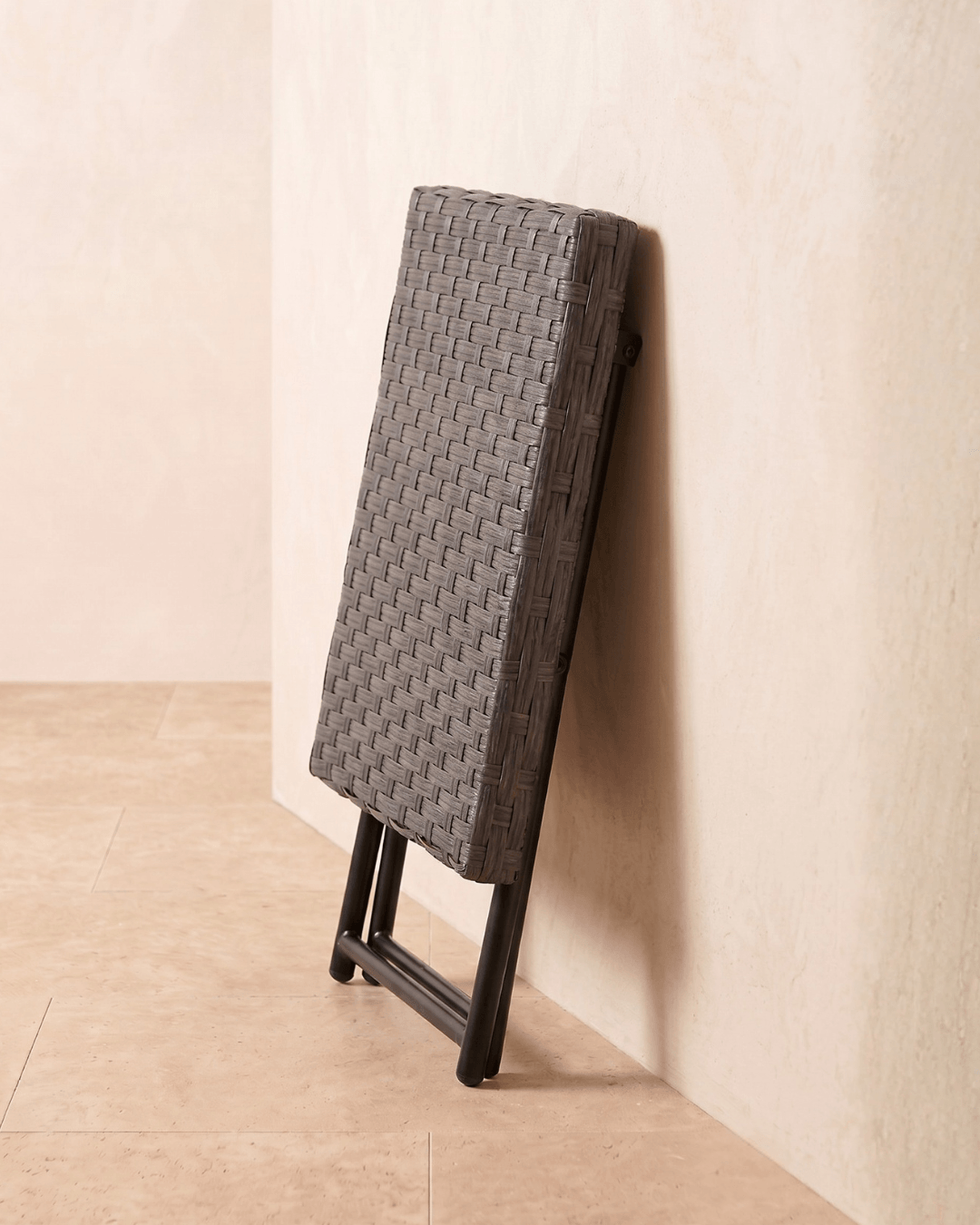 A mountain oak grey rattan side table folded and leaning against the wall