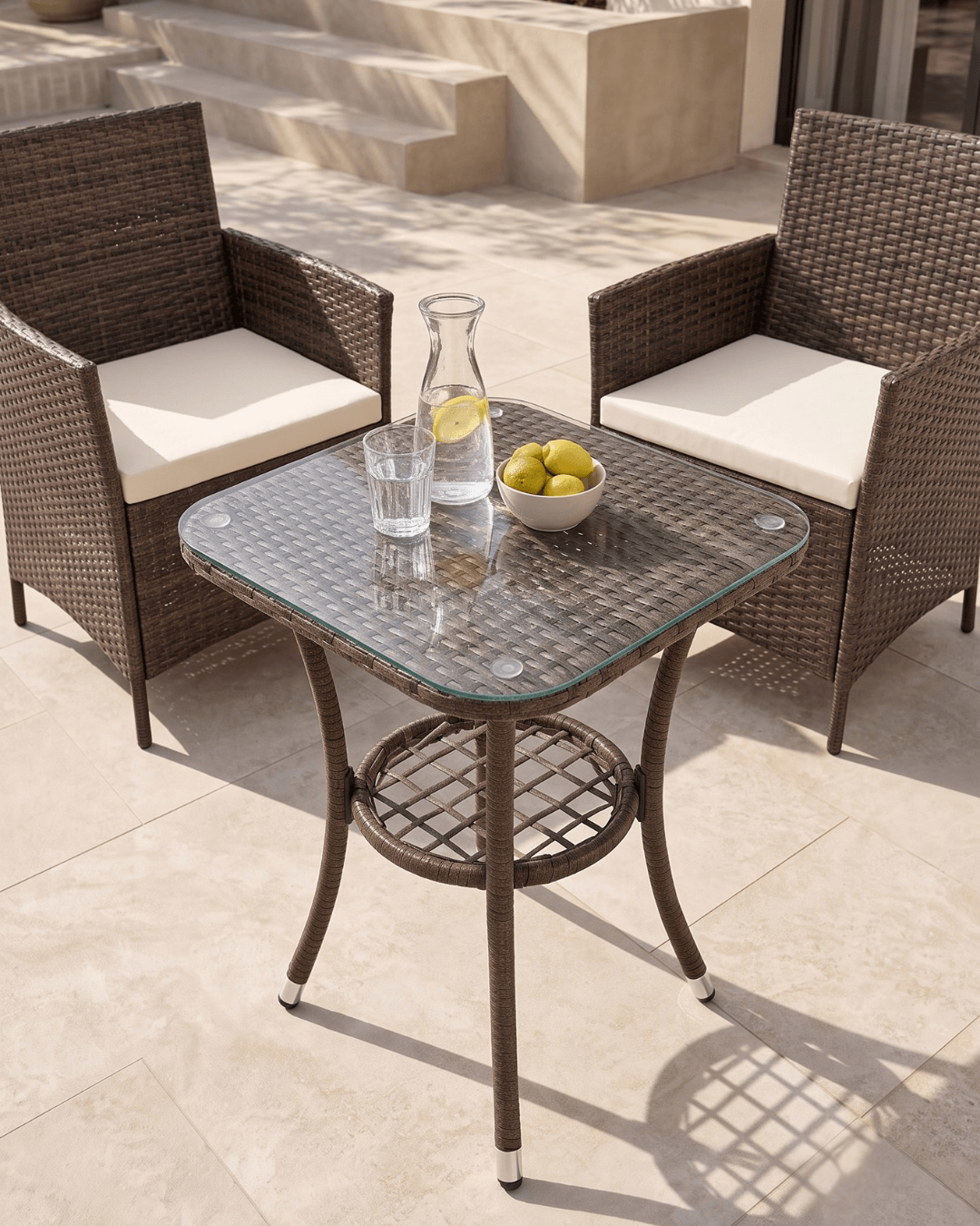 Outdoor patio bistro set featuring a square glass-top table with a brown woven wicker frame, two matching armchairs with cream cushions, and a bistro table
