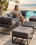 Woman lounging on an outdoor sectional sofa with matching ottomans and a slatted coffee table in a patio setting