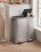 A large silver stainless steel kitchen bin with an open lid, placed on a wooden floor next to a kitchen counter