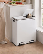 A large white dual kitchen bin with an open lid, placed on a wooden floor next to a kitchen counter