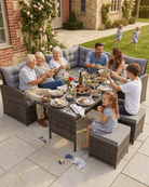 A large outdoor sectional wicker patio set with a matching rattan table, styled with food and surrounded by a family of seven on a stone patio in front of a brick house