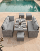 6-piece outdoor patio dining set with a rectangular wicker table, two grey rattan 3-seater sofas and three stools on a beige stone patio next to a swimming pool