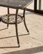 Outdoor patio side table with a woven wicker-style frame, beveled edges, glass top, and lower shelf
