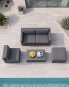A top-down view of a 5-piece outdoor patio conversation set in dark grey wicker, including a rectangular coffee table, arranged on a light stone patio next to a swimming pool