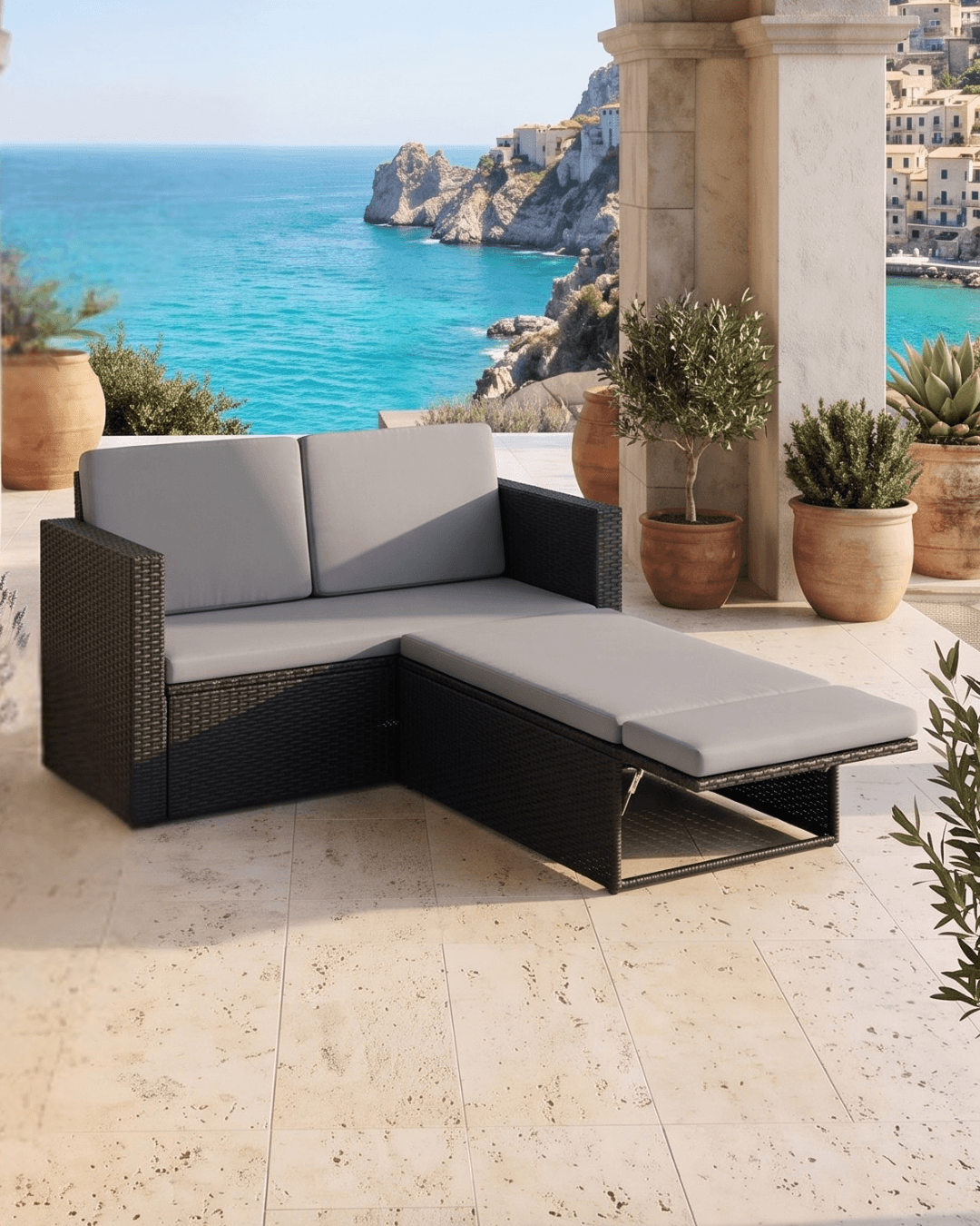 An outdoor sectional sofa with a chaise lounge, featuring black woven wicker frame and light grey cushions, set on a stone patio with a scenic view of the blue sea and cliffs in the background