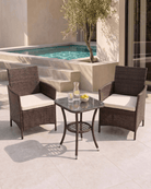 A 3-piece outdoor patio furniture set featuring two brown wicker armchairs with cream cushions and a matching small square glass-top bistro table