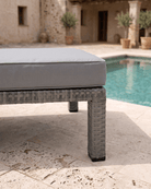 A luxuriously thick cushion on a grey rattan sun lounger positioned on a stone patio next to a swimming pool