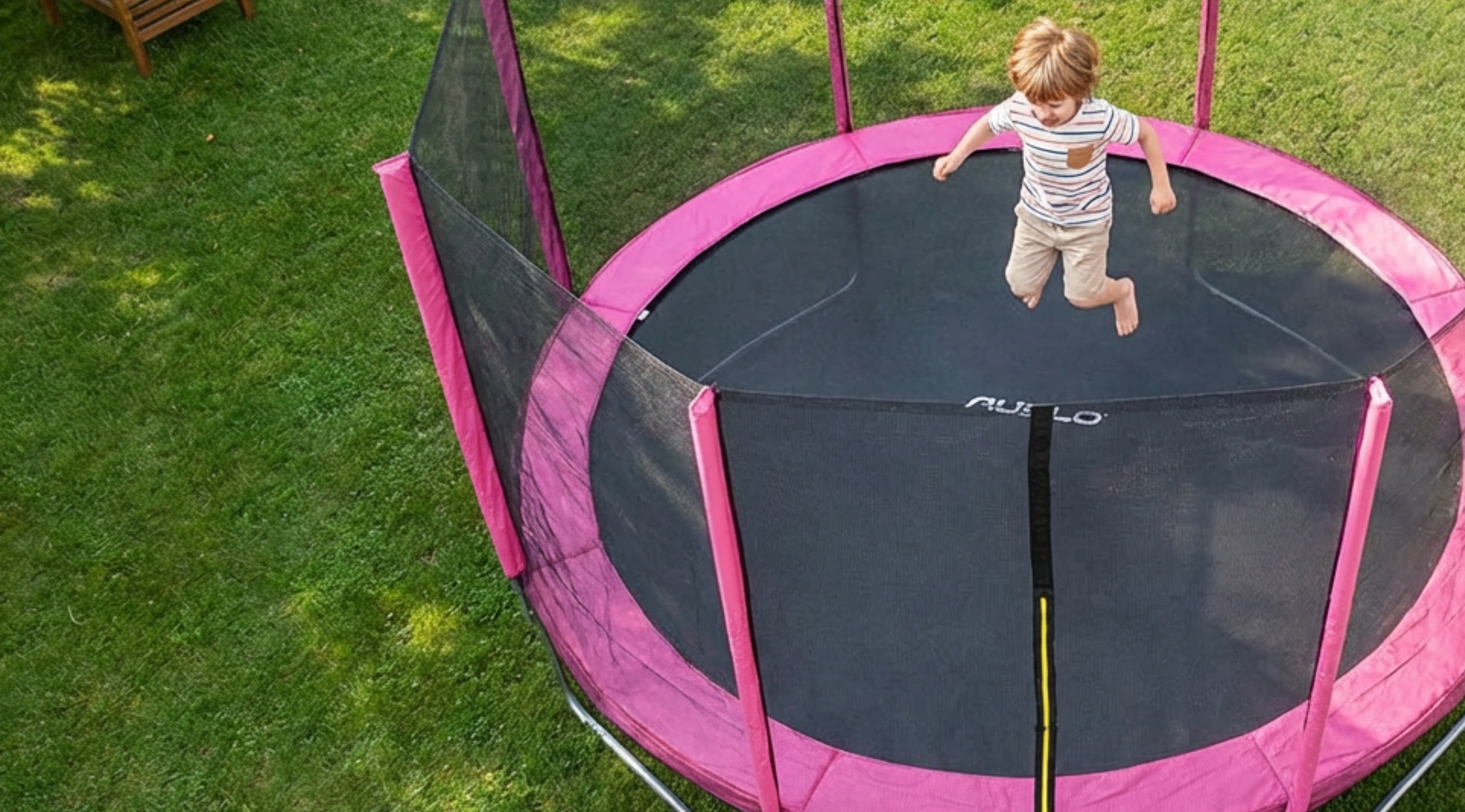 Child jumping on a pink and black trampoline in a grassy area