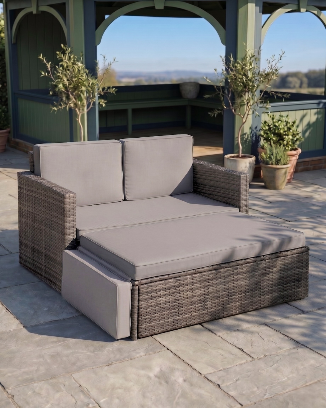Rattan gray outdoor daybed with grey cushions on a stone patio area
