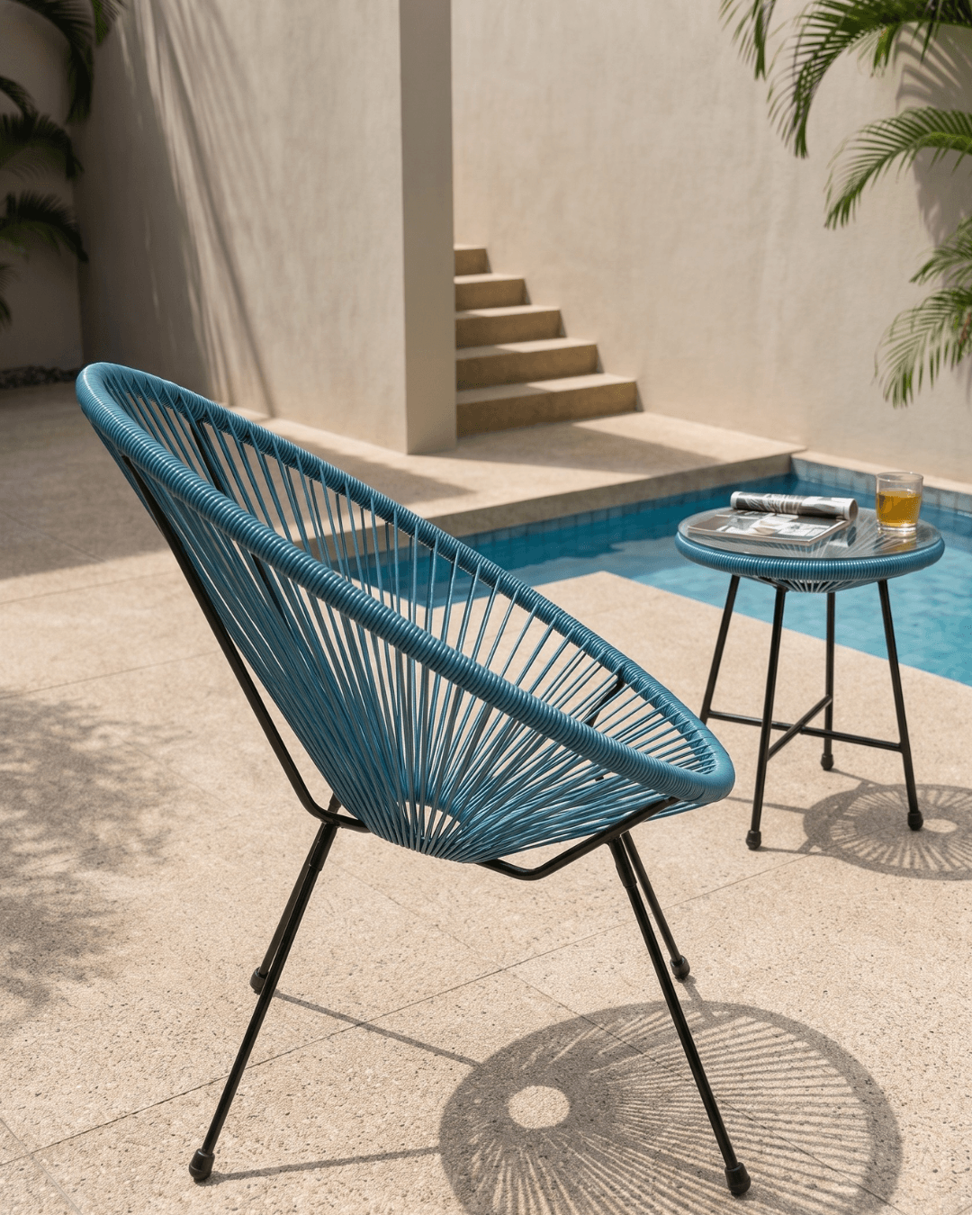 A blue woven egg chair with a black metal frame sits beside a small round side table on a patio