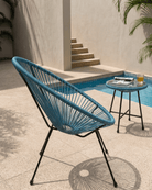 A blue woven egg chair with a black metal frame sits beside a small round side table on a patio