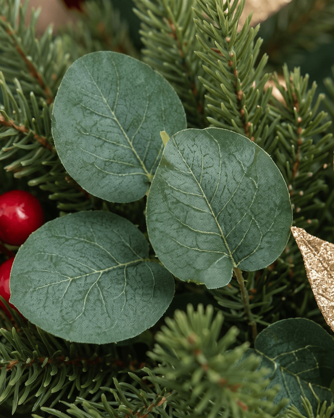 Close-up of faux eucalyptus leaves, pine needles and small red berries on a Christmas wreath
