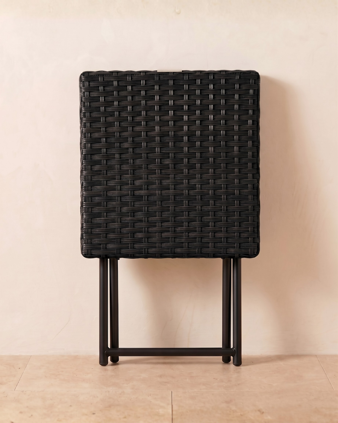Collapsible side table with black rattan tabletop leaning against a wall