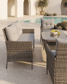 4 seater outdoor garden dining set with woven brown wicker-style chairs and a matching table, styled on a stone patio beside a swimming pool