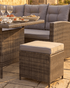 Outdoor wicker patio furniture set including a rectangular table, a large corner sofa, and a matching ottoman, arranged on a stone patio