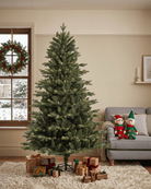 A 7ft tall artificial Christmas tree stands in a living room next to a window with a wreath, with wrapped gifts underneath