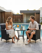 Two people sitting at a black rattan bistro set, enjoying drinks and conversation