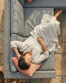 Person lying on a grey outdoor corner sofa with pink cushions