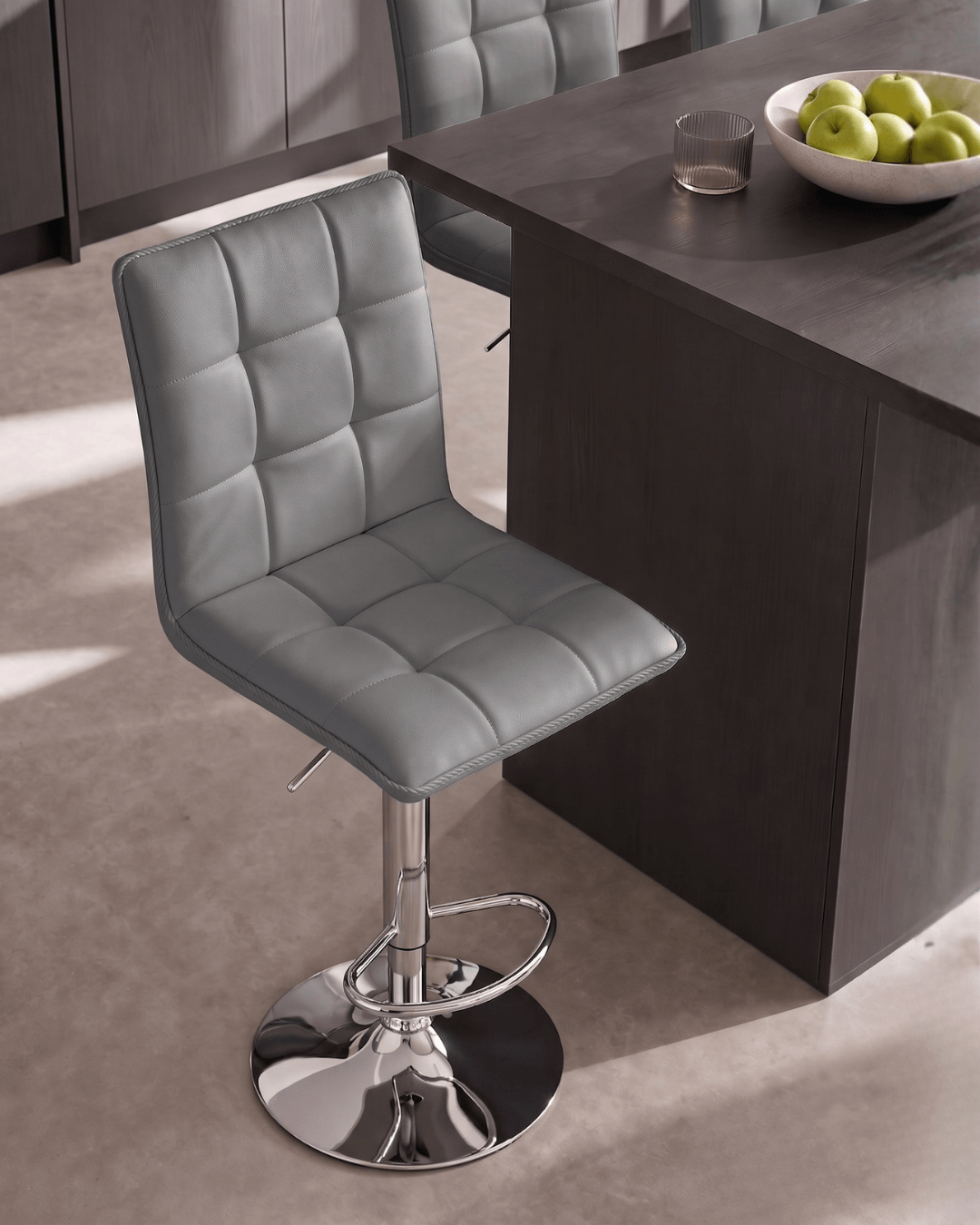 A modern bar stool with a grey upholstered seat mounted on a chrome pedestal base