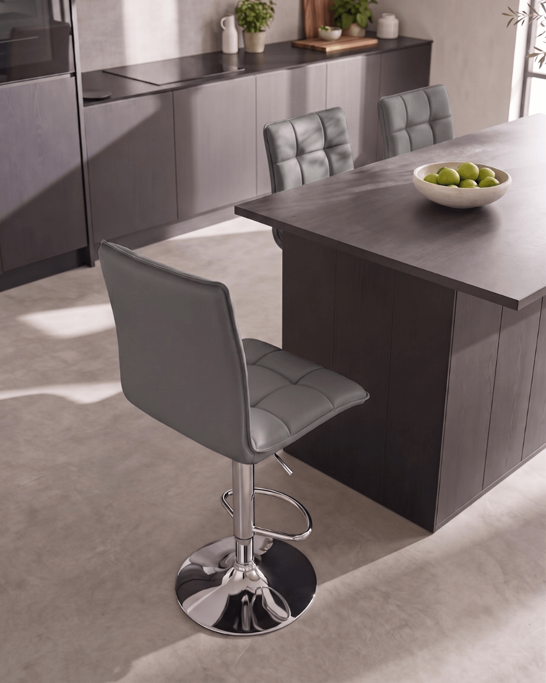 A modern kitchen scene featuring grey faux leather bar stools with a chrome pedestal base