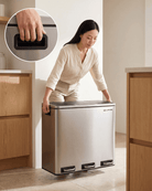 Woman lifting and repositioning a stainless steel bin with recycling compartments in a modern kitchen