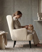 Woman sitting in a luxury cream lounge chair wingback with a cat on her lap in a cosy room