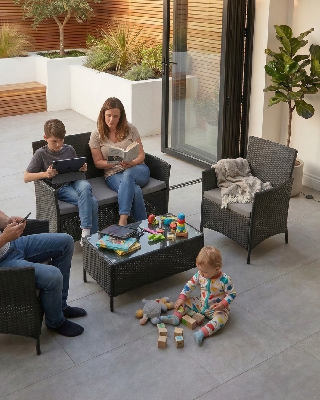 Family sitting outdoors on black patio furniture with children playing nearby
