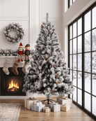 A large snow-flocked Christmas tree by a fireplace and floor-to-ceiling windows