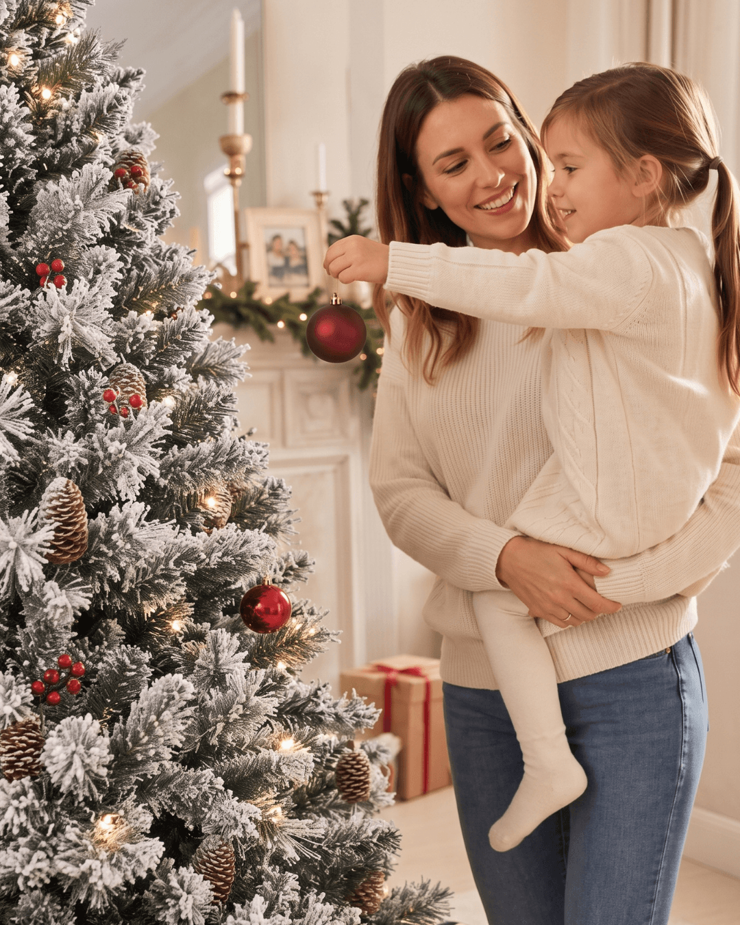 Mother and daughter decorating a tall snowy white Christmas tree with pine cones and berries