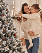 Mother and daughter decorating a tall snowy white Christmas tree with pine cones and berries